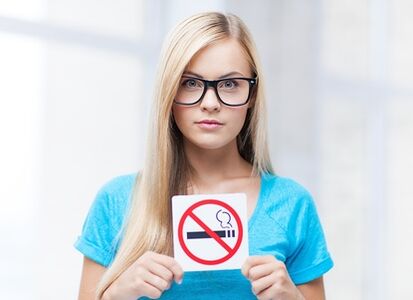 mergina prie įėjimo laiko ženklą, draudžiantį rūkyti
